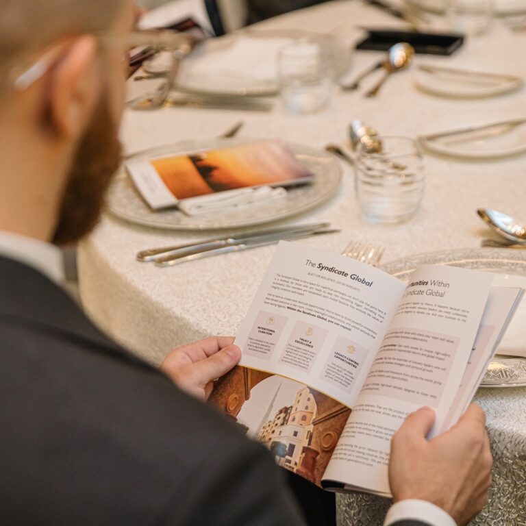 Attendee reading the event brochure at the dining table during The Syndicate Global luxury event in Dubai