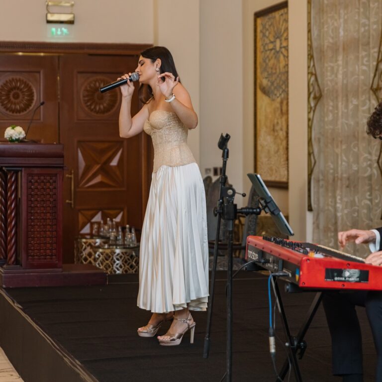 Female singer Alina Bashkina performing on stage with a live keyboard player at The Syndicate Global event in Dubai.